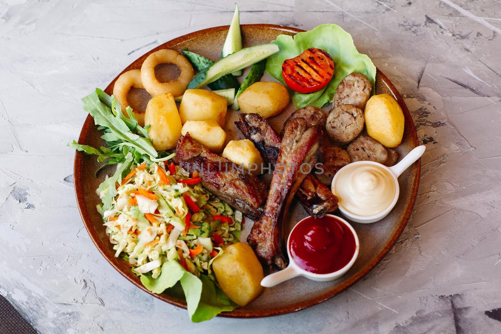 Delicious restaurant appetizers set for beer. vegetable salad, boiled potatoes, grilled chicken legs, roasted onion, sausages, cucmbers, tomatoes and sauces - ketchup and mayo laying on clay plate.