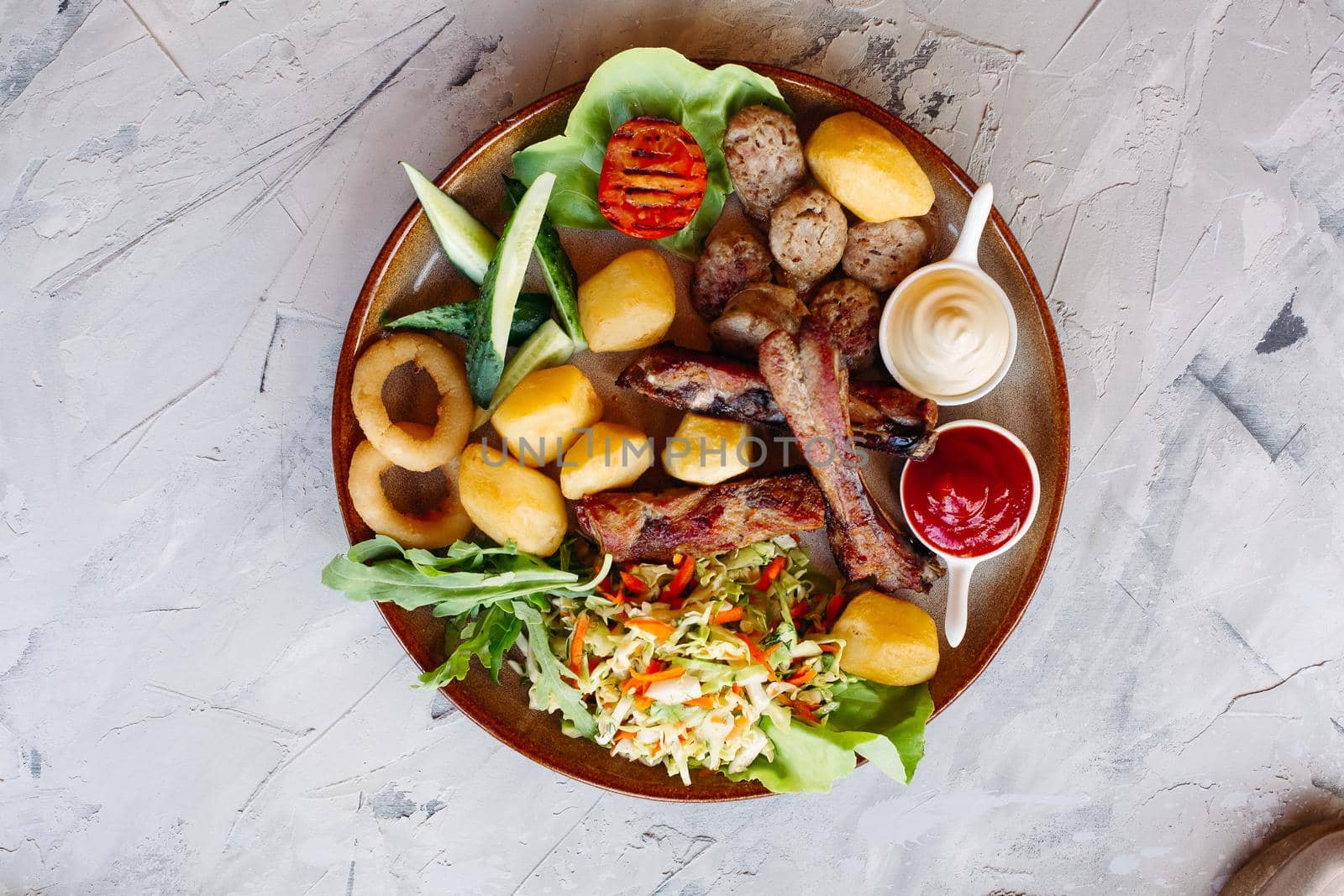 Delicious restaurant appetizers set for beer. vegetable salad, boiled potatoes, grilled chicken legs, roasted onion, sausages, cucmbers, tomatoes and sauces - ketchup and mayo laying on clay plate.