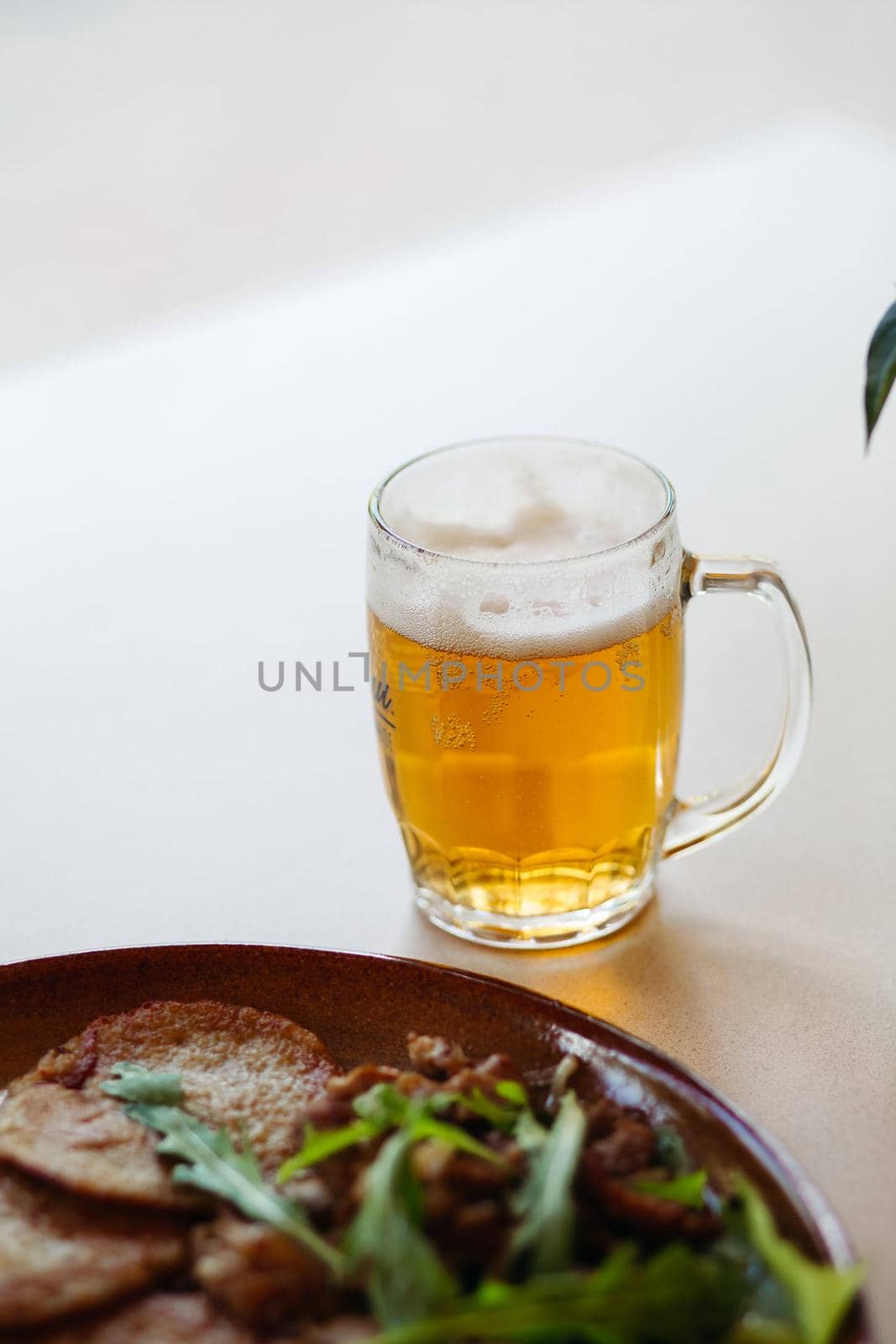 Horizontal photo of glass cup full of light fresh beer standing on smooth wooden surface. Cold summer drink for day heat. Fresh with thick high foam. Blurred background. Concept of drinks shooting.