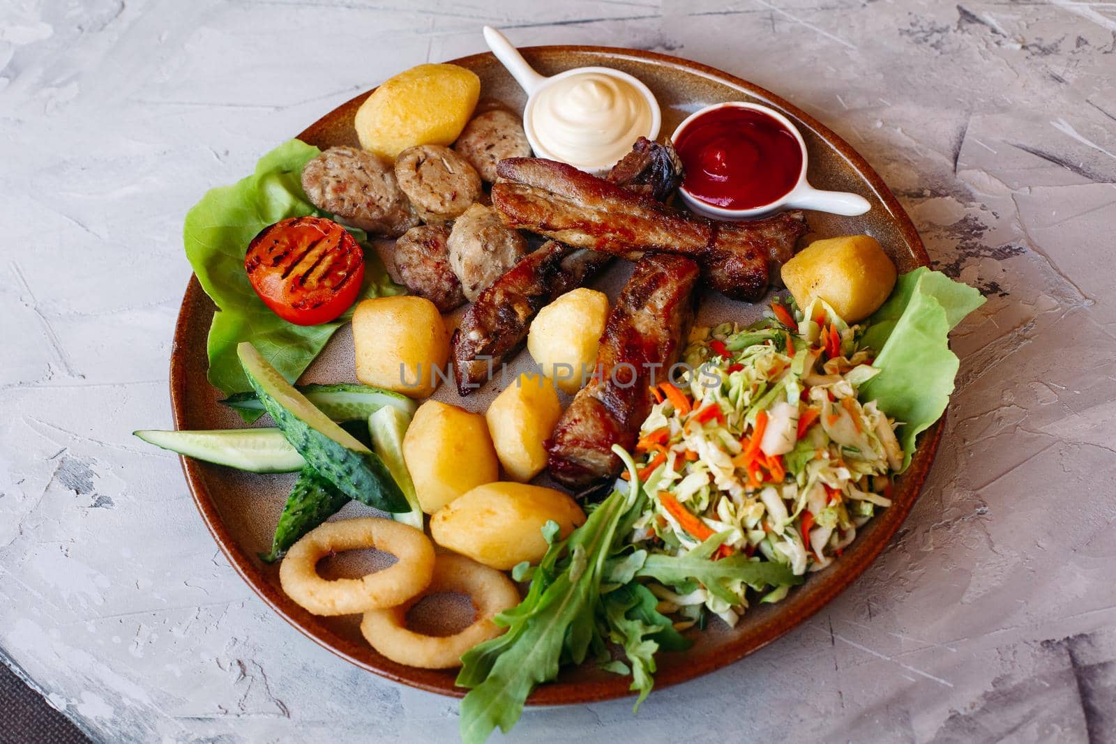 Delicious restaurant appetizers set for beer. vegetable salad, boiled potatoes, grilled chicken legs, roasted onion, sausages, cucmbers, tomatoes and sauces - ketchup and mayo laying on clay plate.