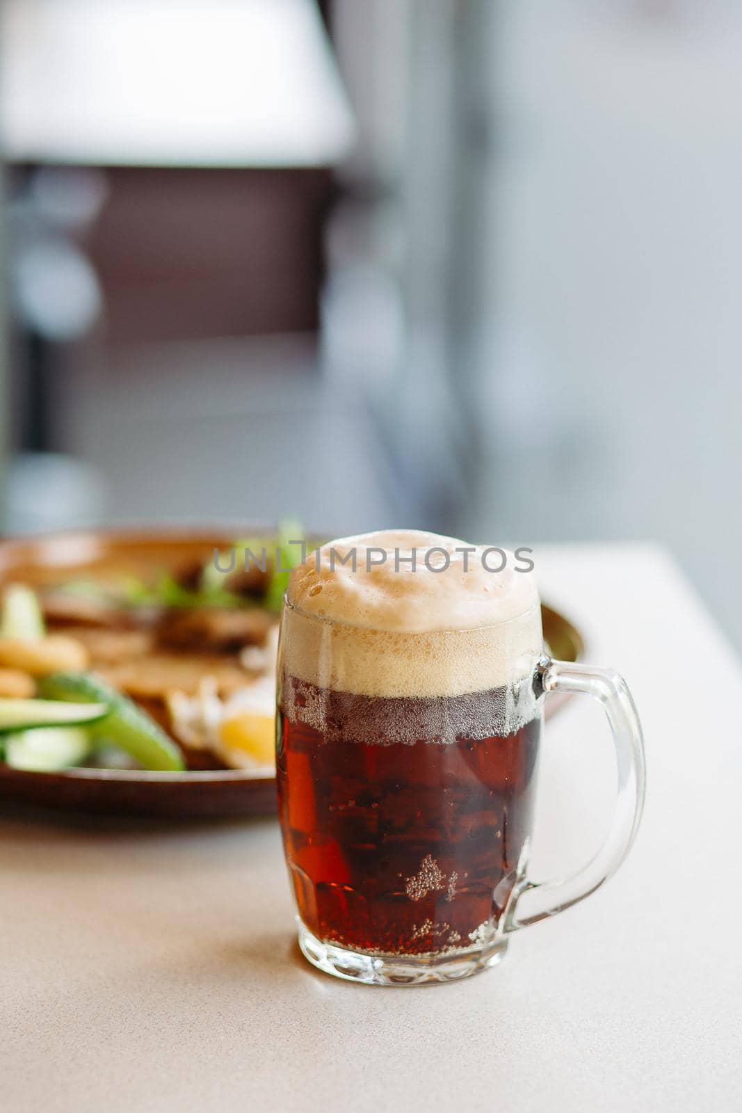 Beer cup standing near appetizers plate. Dark beer with thick high foam. Standing on smooth wooden surface of restaurant's or pub table. Looking mouthwatering. Cold and fresh. For friends company.