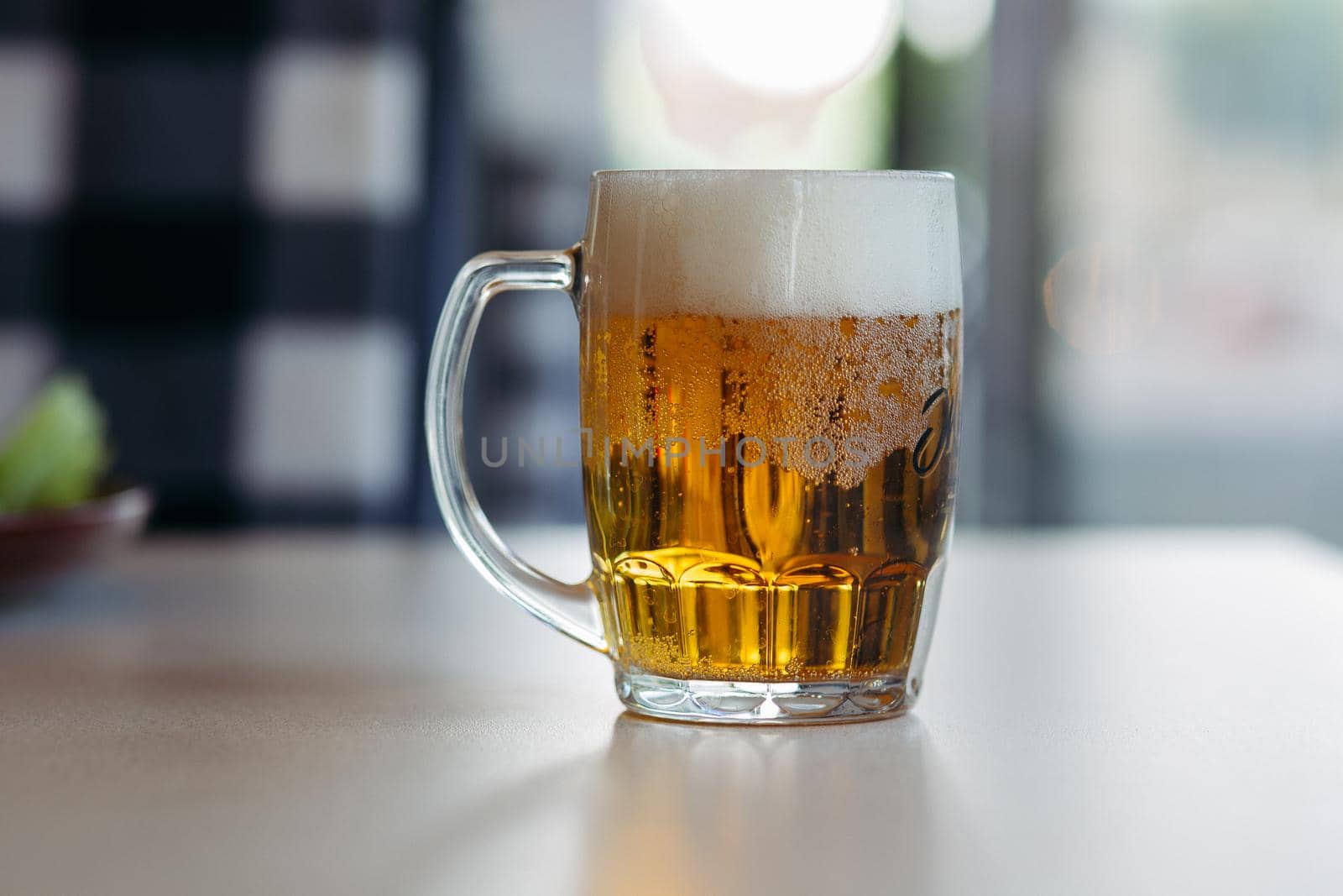Horizontal photo of glass cup full of light fresh beer standing on smooth wooden surface. Cold summer drink for day heat. Fresh with thick high foam. Blurred background. Concept of drinks shooting.