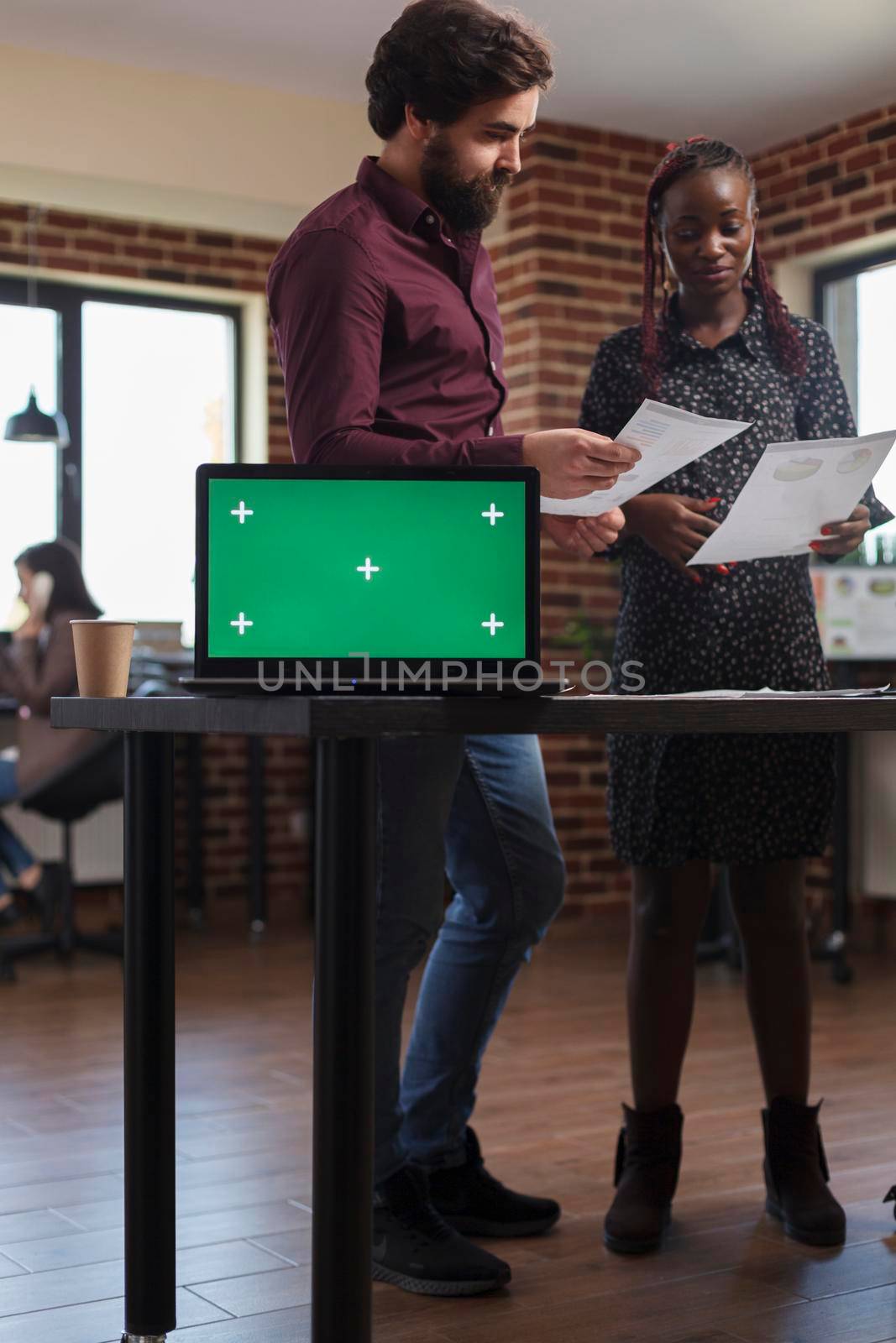 African american pregnant businesswoman and coworker looking over company accounting documentation. Marketing agency desk with isolated background and mockup template on computer.