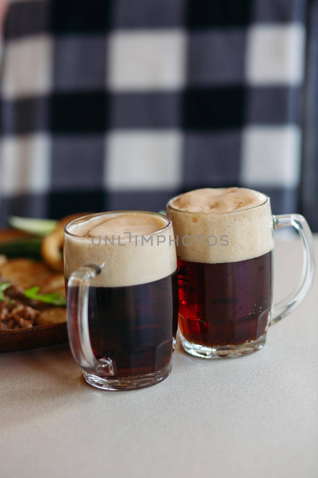 Two big glass cups full of foamy cold beer standing on light smooth table surface in restaurant or pub. Big plate with delicious appetizers like potato puncakes and fried eggs standing on background.