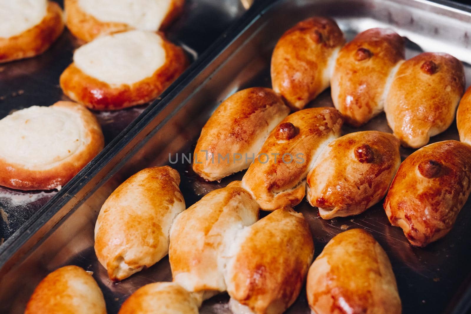 Delicious fresh baked flavored buns set made of sweet dough laying on big metallic dish standing in bakery kitchen. Looking mouthwatering, tasty. Laying near warm buns with cottage cheese feeling.