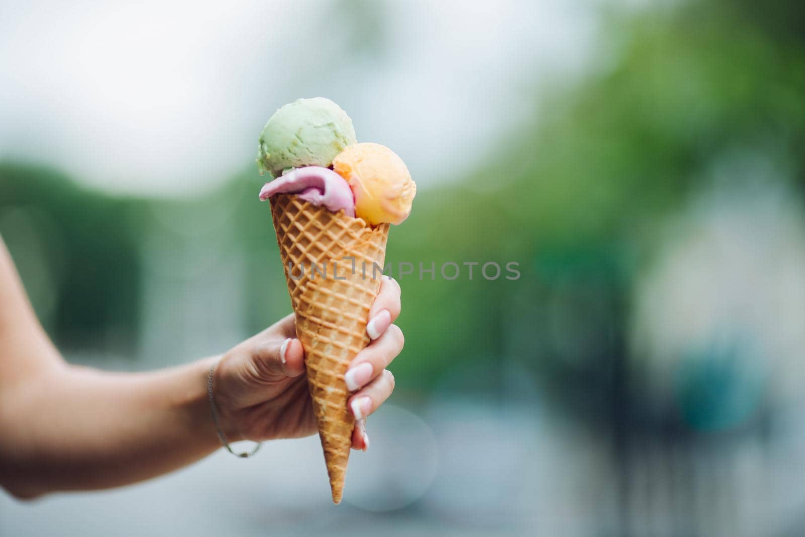 Crop of woman's hand holding delicious colorful ice cream with three colors. Close up of tasty, sweet, mouthwatering, perfect for summer heat while sunny day. Summertime vibes and sweet food.