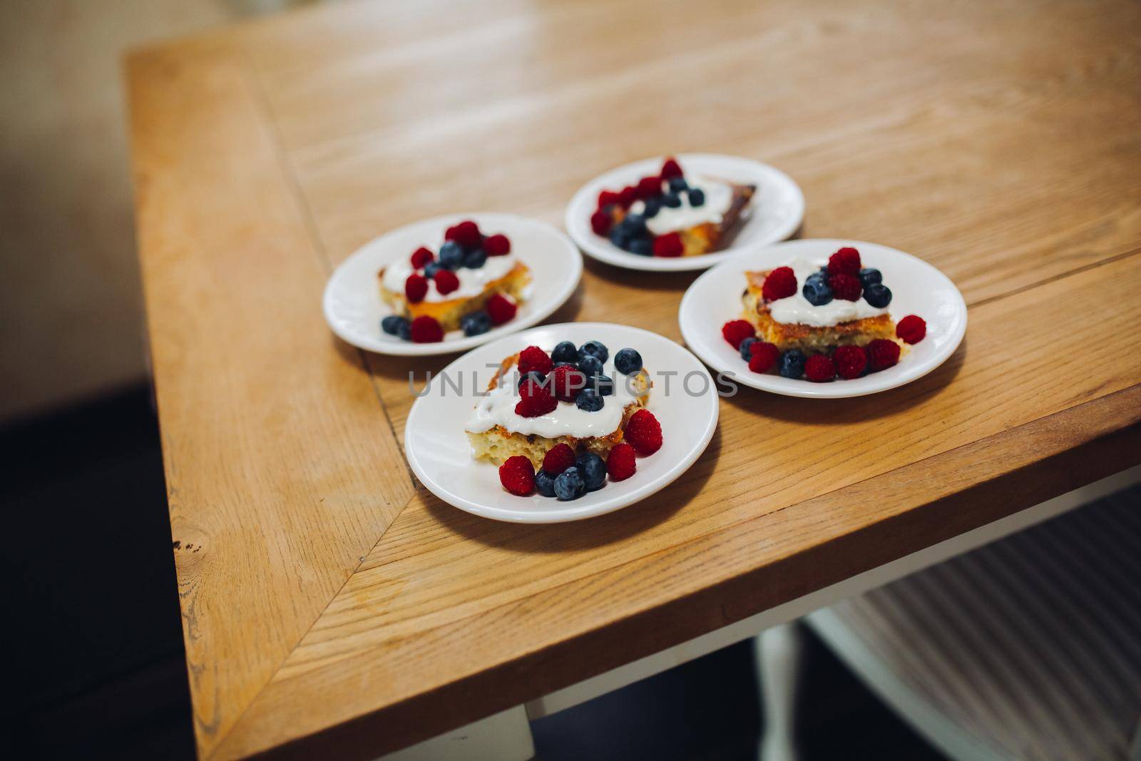 View of tasty and fresh breakfast in cafe, four portion of sweet bake with different berries. Home made desert with raspberry, blueberry and cream on wooden table. Concept of family breakfast.