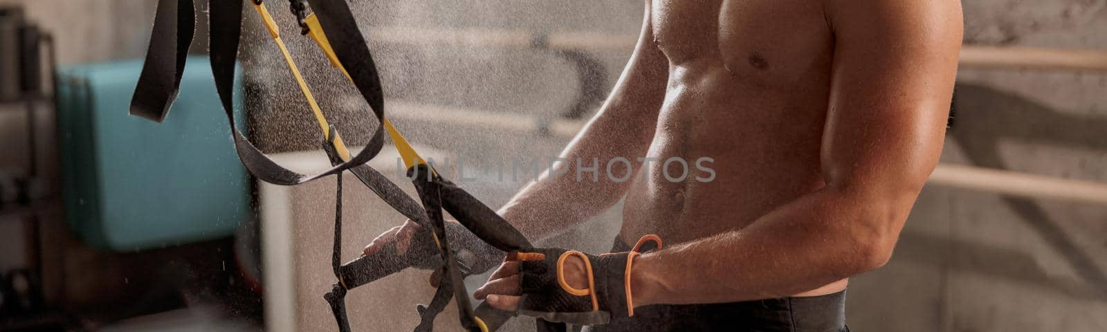 Muscular male in training gloves holding fitness straps in the sport club, smiling