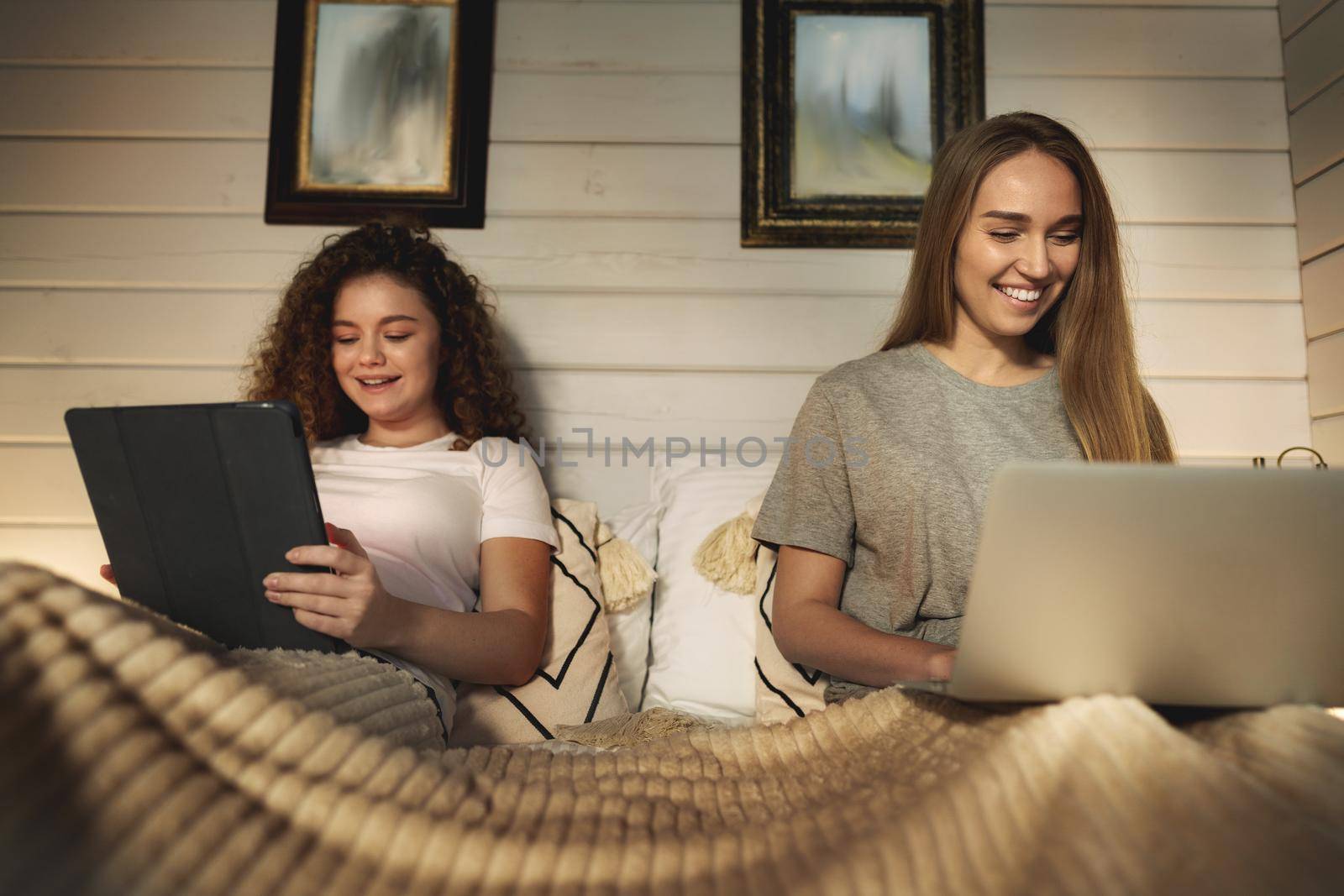 Two beautiful women lying in bed, holding and watching laptop