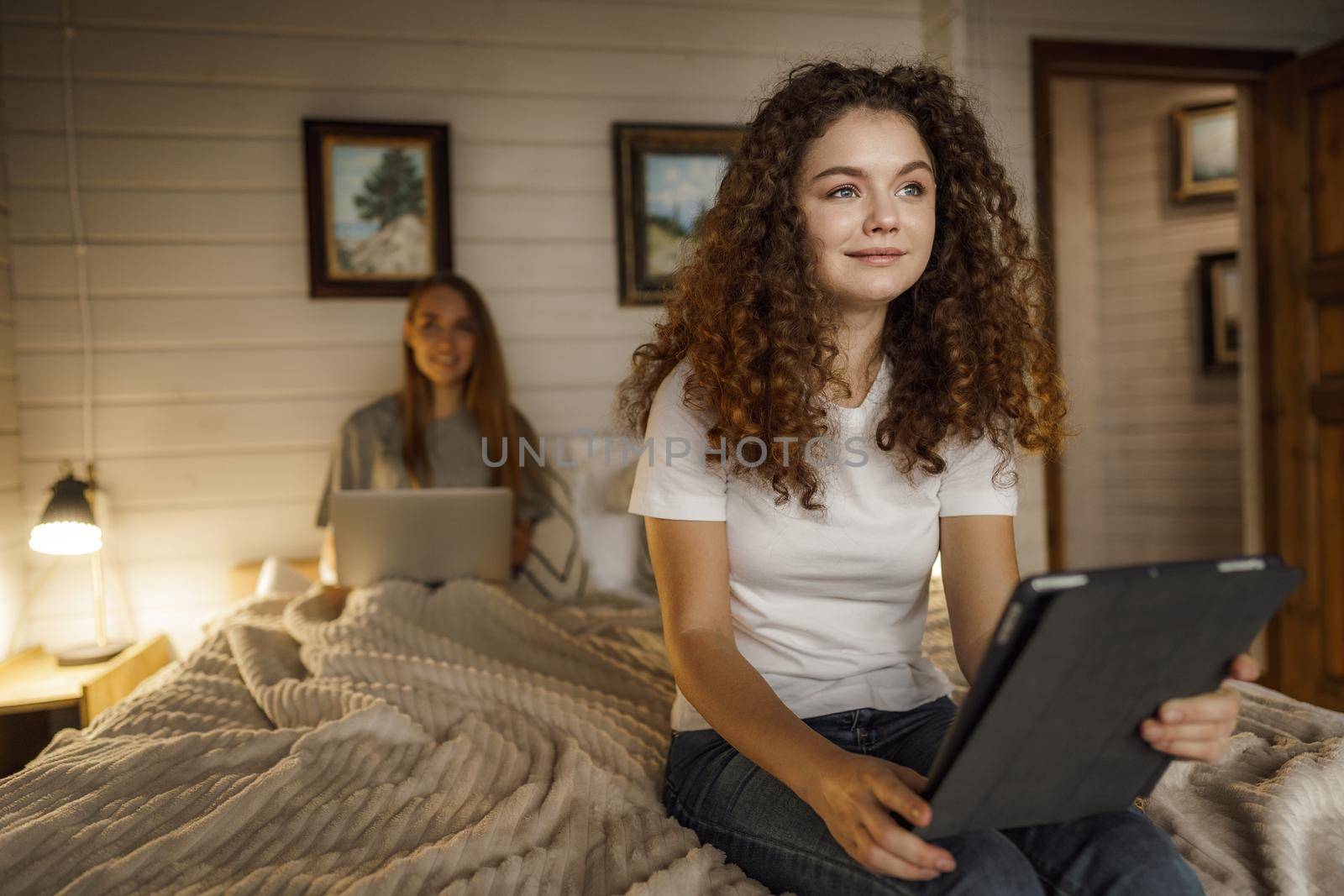 Two beautiful women lying in bed, holding and watching laptop