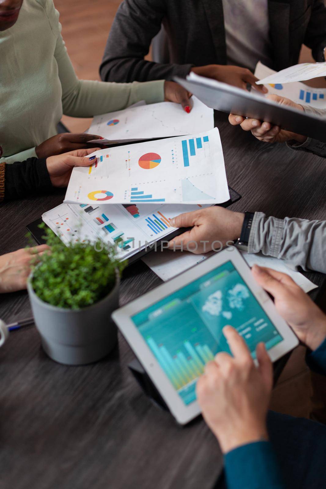 Closeup of businessman holding tablet computer with marketing graphs on screen. Multiethnic businesspeople working at marketing project sharing papers with company turnover during business meeting