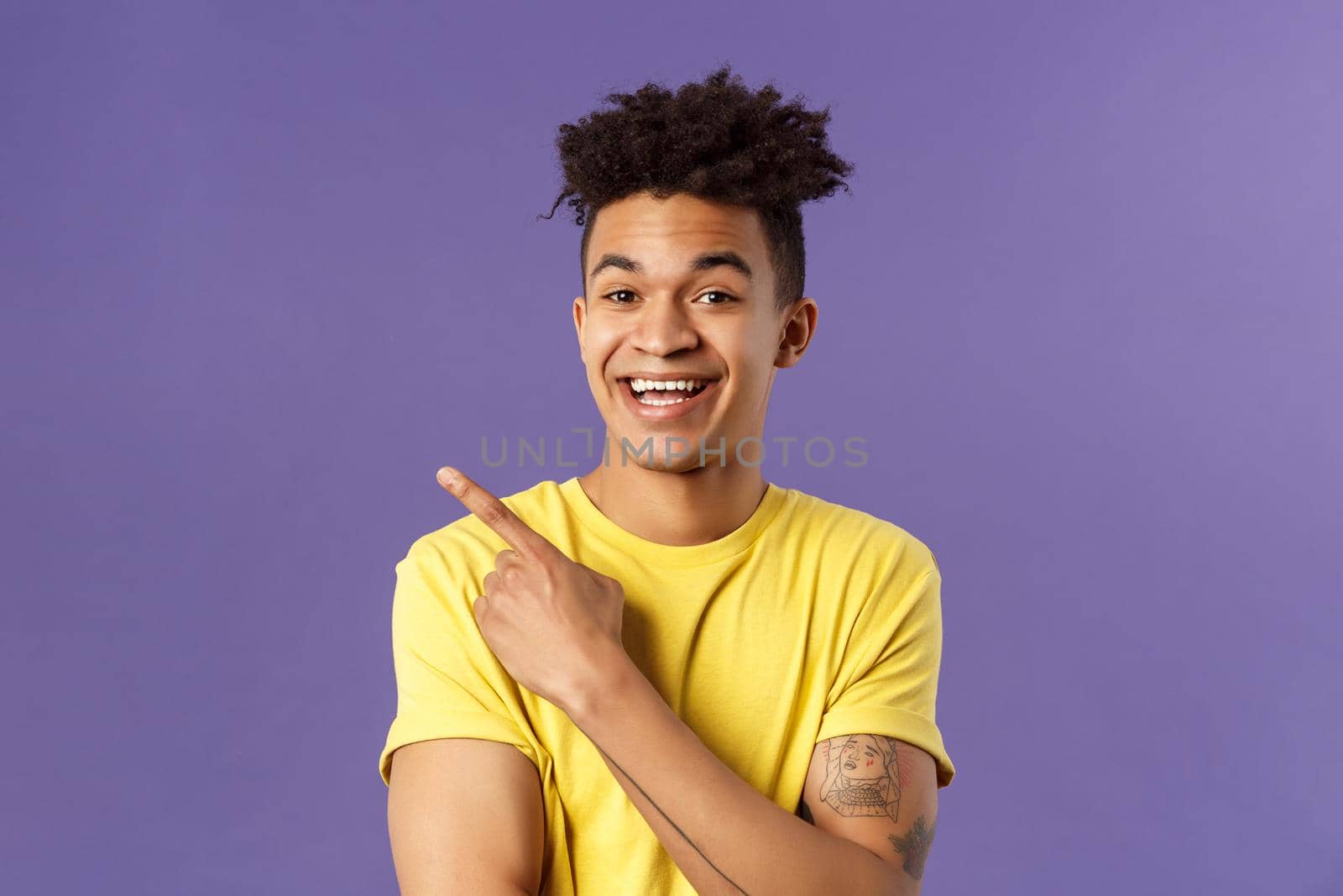 Close-up portrait of cheerful, attractive young male student showing promo, pointing at upper left corner, smiling pleased, recommend click link, visit page or download app, purple background by Benzoix