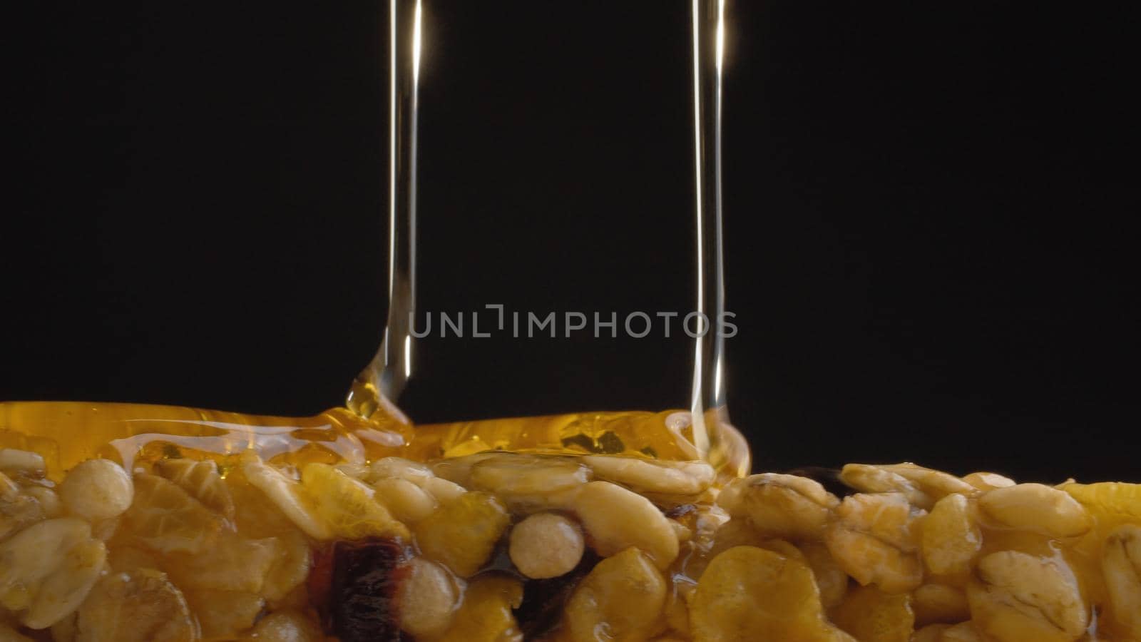 Extreme close up fresh honey pouring on a cereal bar, muesli on black background. Healthy energy fitness food