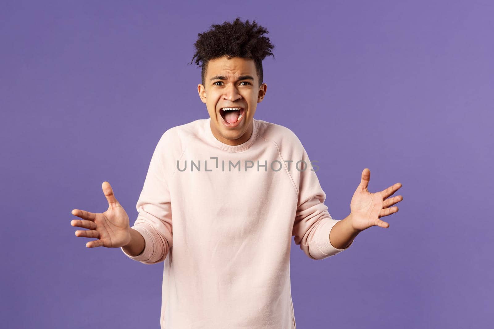 Portrait of concerned, upset and frustrated young man cant believe he lost, asking why, spread hands sideways in dismay, complaining shouting angry and uneasy, standing purple background.