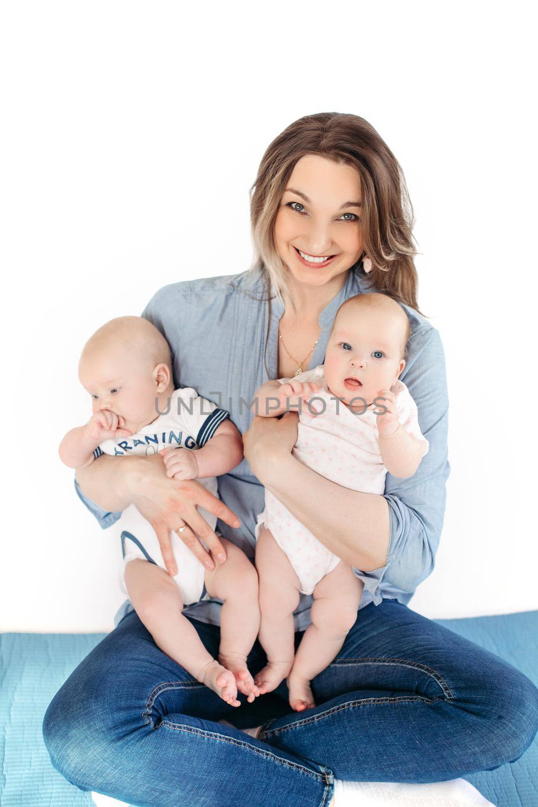 Picture of cheerful young caucasian female sits with her children, smiles and hugs them