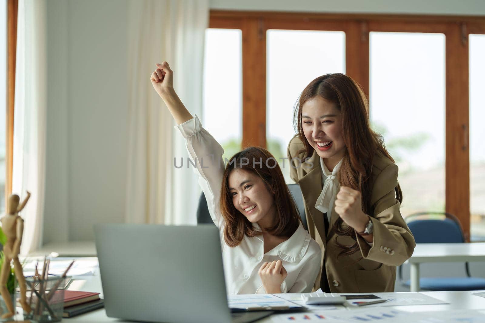 Happy young business asian team looking at laptop screen, celebrating success, Raising arms in a celebration of a successful
