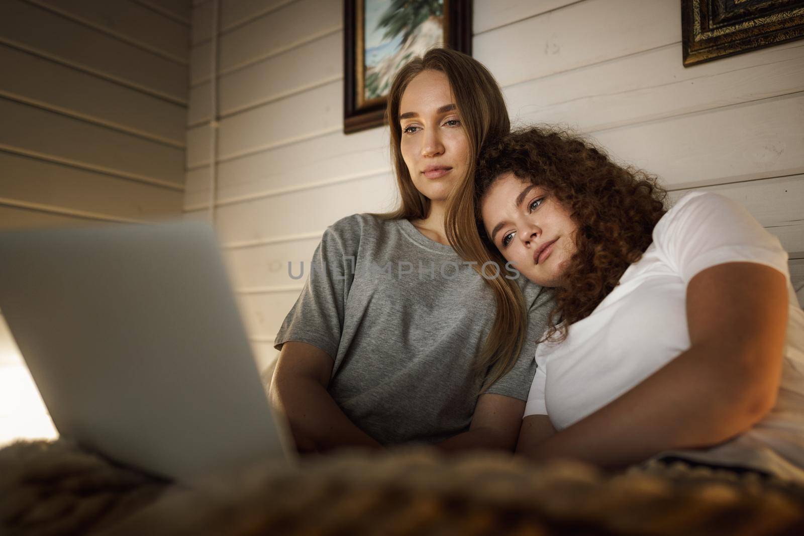 Two beautiful women lying in bed and watching movies on laptop at home