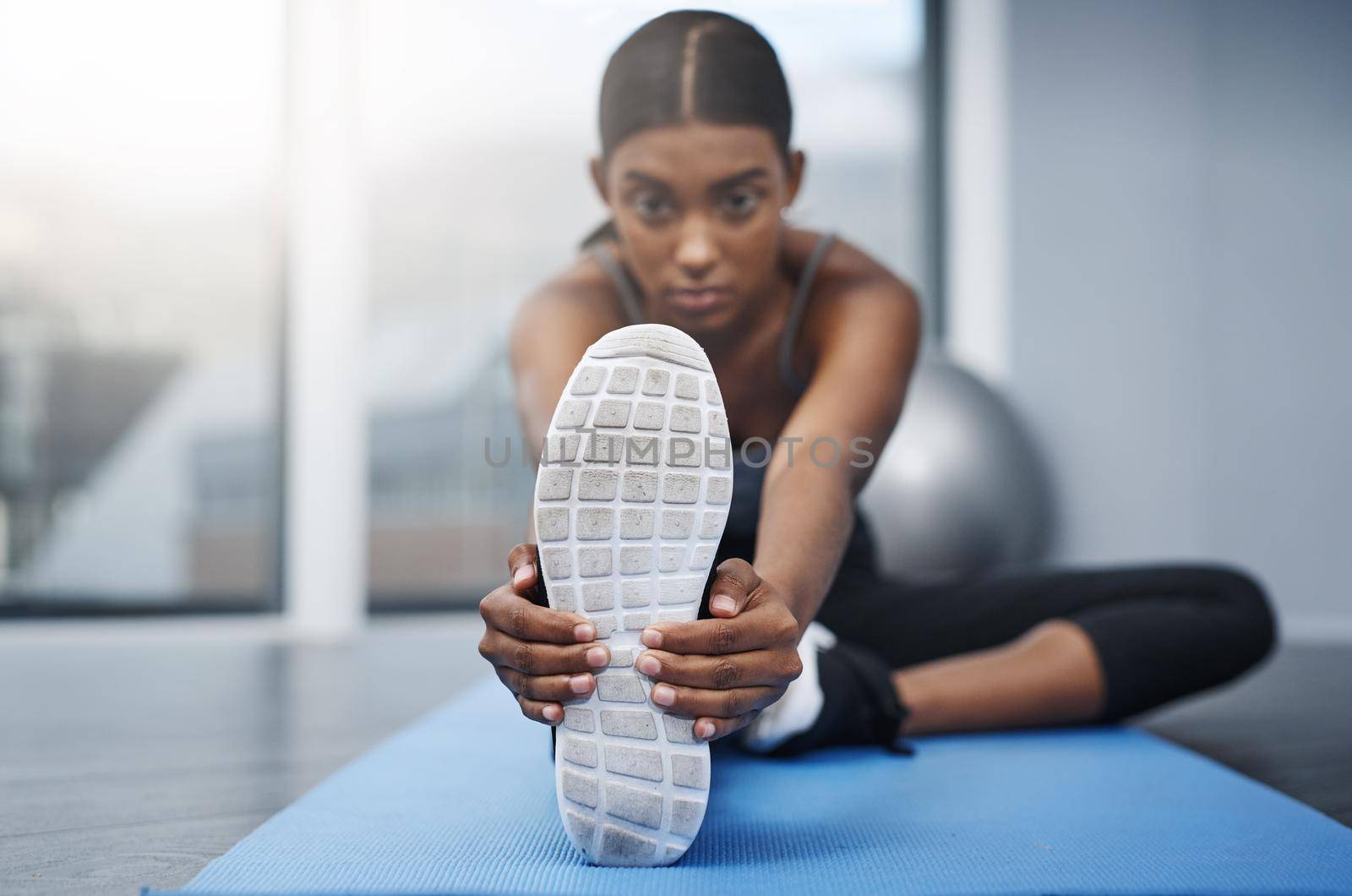 Shot of an attractive young woman sitting down and doing stretching exercises on her gym mat at home.
