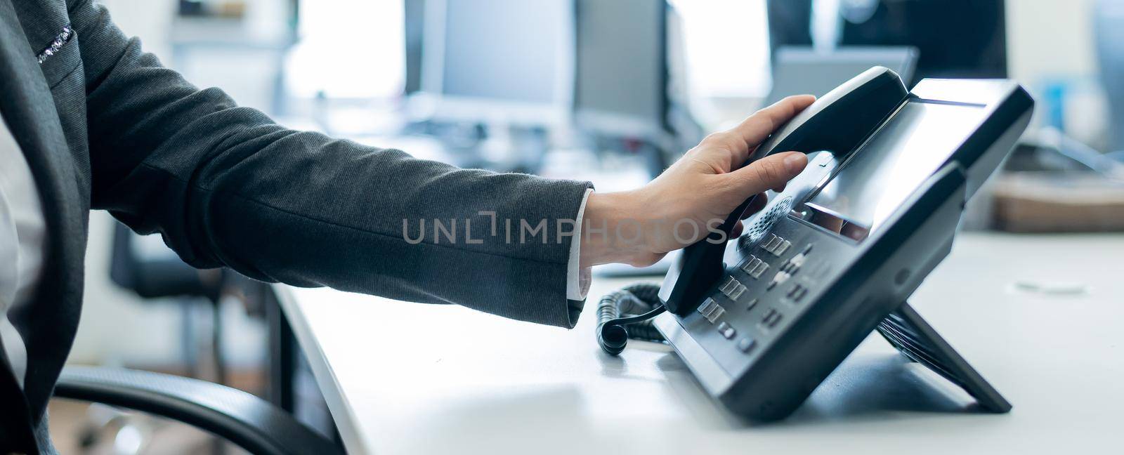 Close-up of a female employee's hand on a landline phone. Woman picks up a push-button telephone at the workplace in the office.