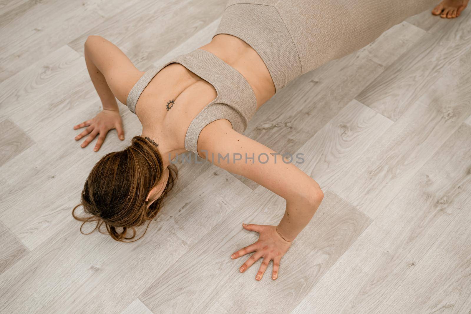 Top view of a muscular woman during push-ups. She is wearing a beige top and leggings, with a round tattoo between her shoulder blades. The concept of a healthy lifestyle