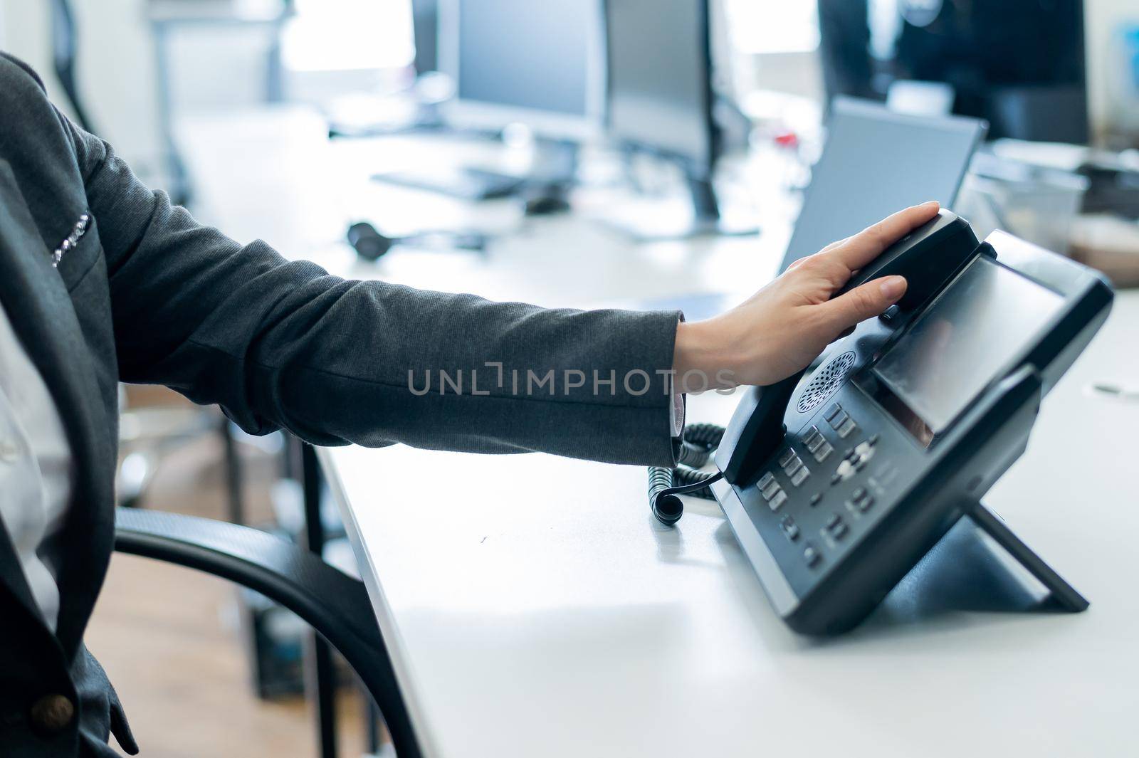 Closeup female hand on landline phone in office. Faceless woman in a suit works as a receptionist answering the phone to customer calls. by mrwed54