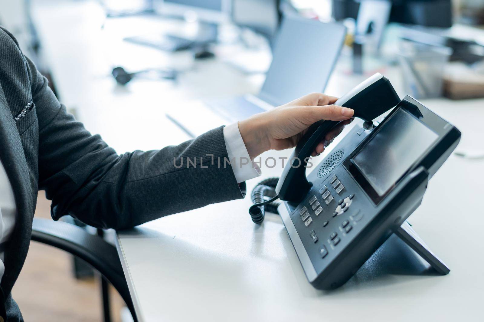 Closeup female hand on landline phone in office. Faceless woman in a suit works as a receptionist answering the phone to customer calls