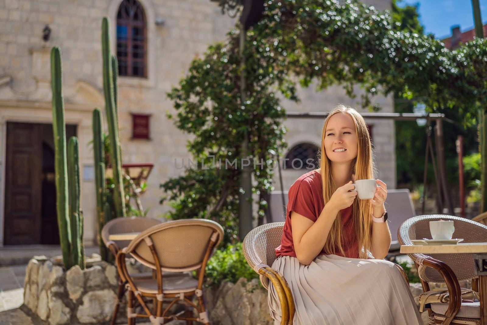 Young woman tourist drinks cofee in the old town of Budva. Travel to Montenegro concept.