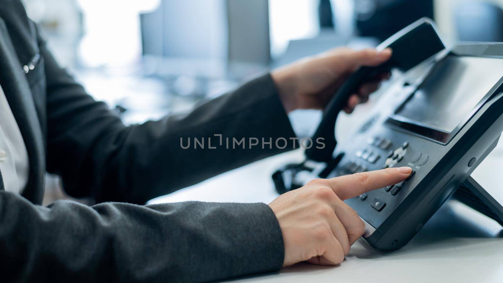 Closeup female hand on landline phone in office. Faceless woman in a suit works as a receptionist answering the phone to customer calls. by mrwed54