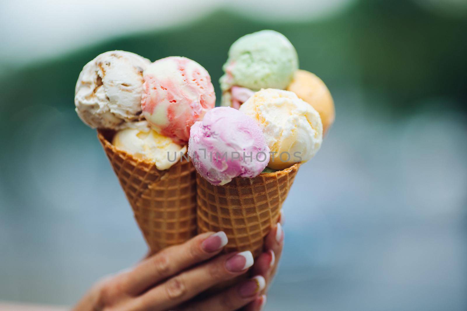 Crop of woman's hand holding delicious colorful ice cream, looking tasty, sweet, mouthwatering, perfect for summer heat while sunny day. Pretty nails with professional french manicure. Food concept.