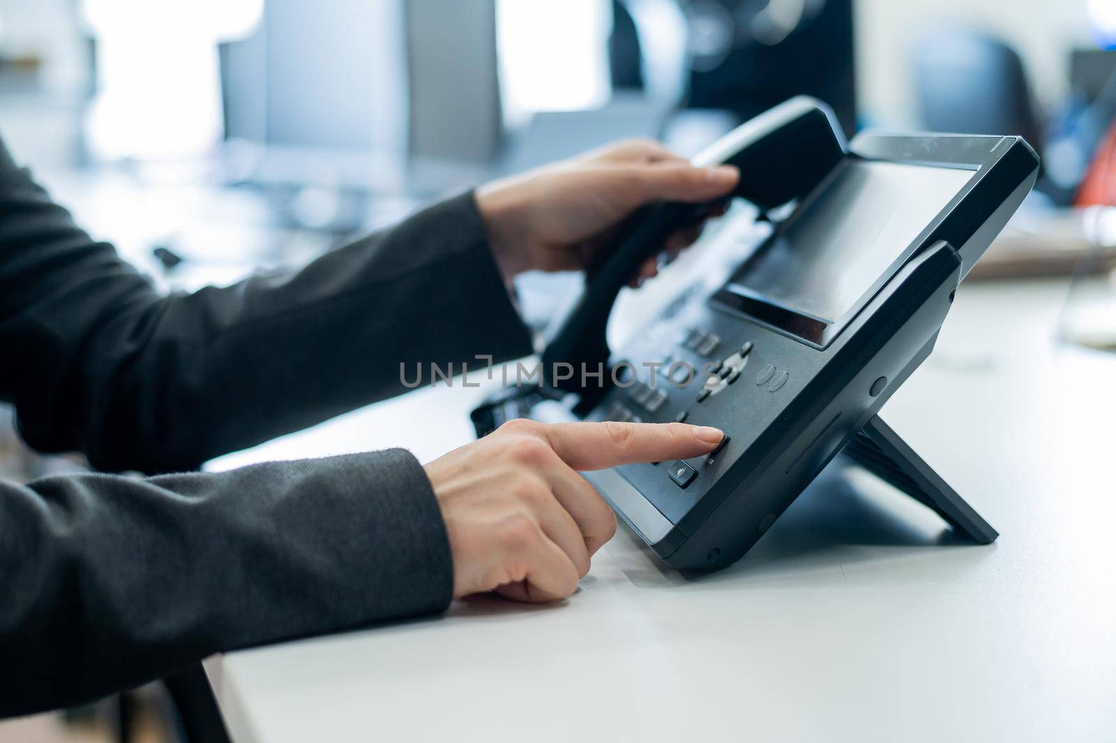 Closeup female hand on landline phone in office. Faceless woman in a suit works as a receptionist answering the phone to customer calls