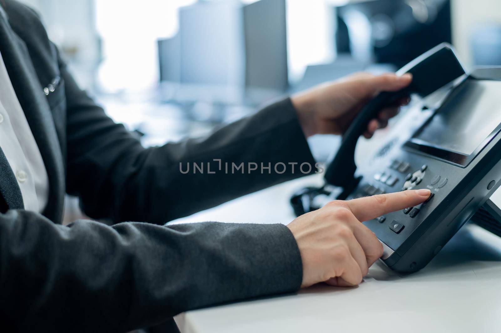 Closeup female hand on landline phone in office. Faceless woman in a suit works as a receptionist answering the phone to customer calls