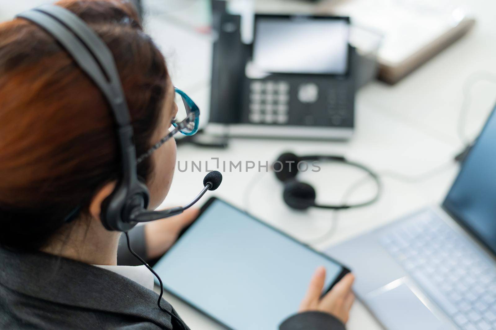 Rear view of a woman in a headset using a digital tablet while sitting at a desk. Friendly female support service operator at work. by mrwed54