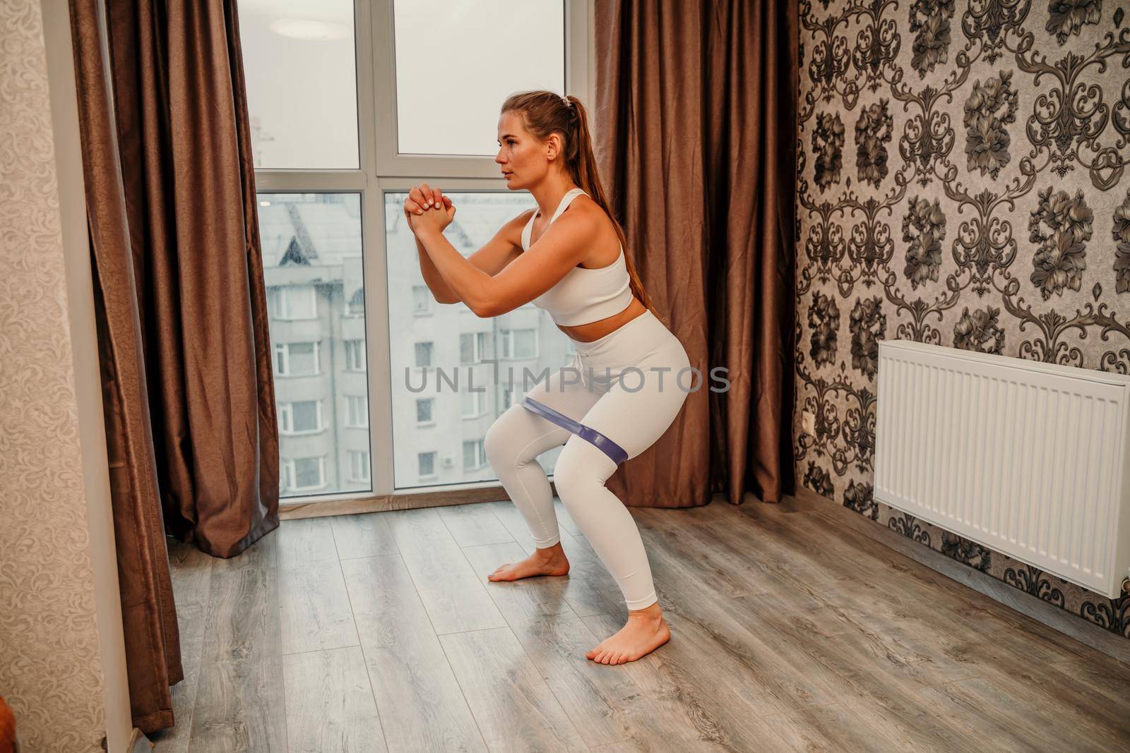 Middle aged athletic attractive woman practicing yoga. Works out at home or in a yoga studio, sportswear, white pants and a full-length top indoors. Healthy lifestyle concept.