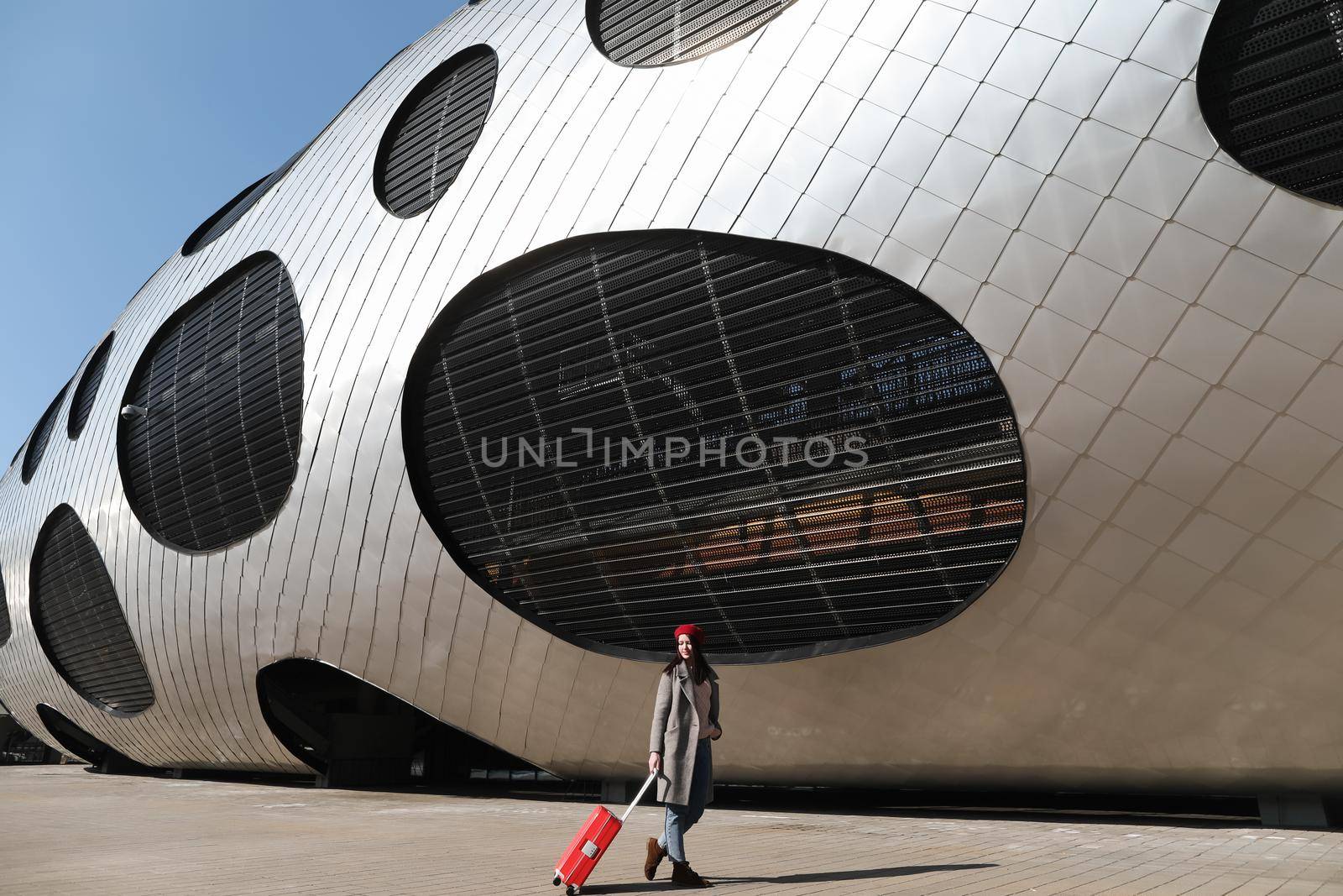 young woman with a red travel suitcase by the futuristic facade of modern architecture. Travel concept