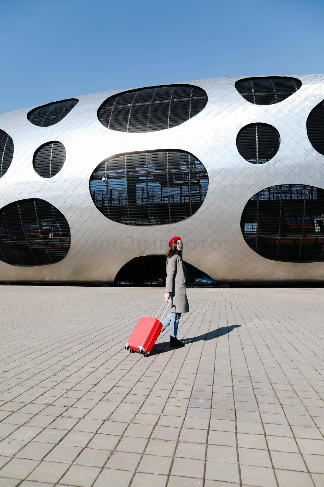 young woman with a red travel suitcase by the futuristic facade of modern architecture. Travel