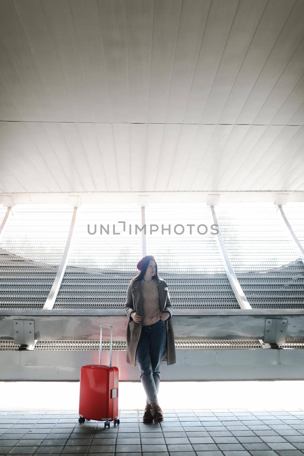 young woman with a red travel suitcase by the futuristic facade of modern architecture. Travel