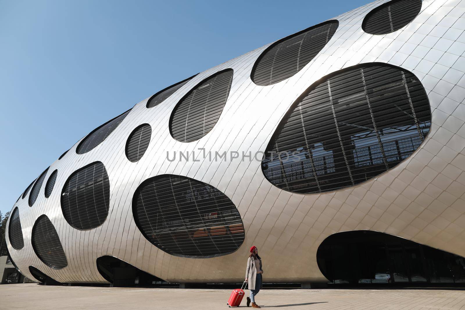 young woman with a red travel suitcase by the futuristic facade of modern architecture. Travel