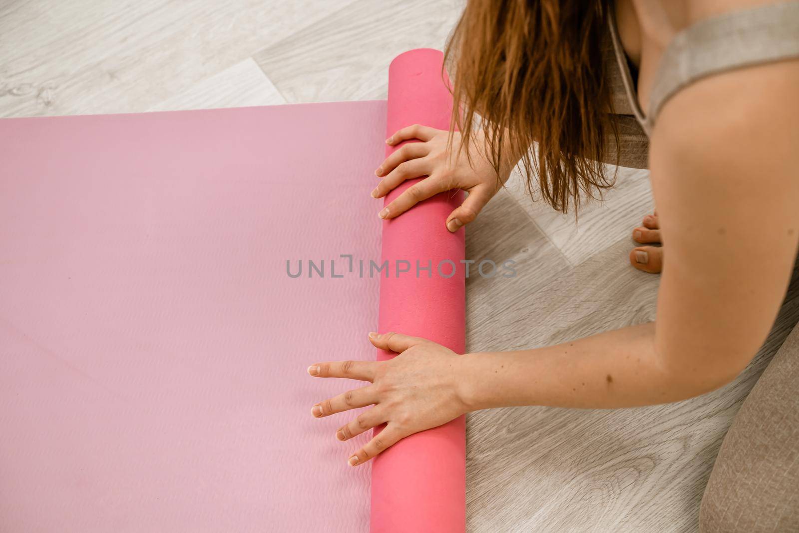 A young woman rolls a pink fitness or yoga mat before or after exercising, exercising at home in the living room or in a yoga studio. Healthy habits, keep fit, weight loss concept. Closeup photo by Matiunina