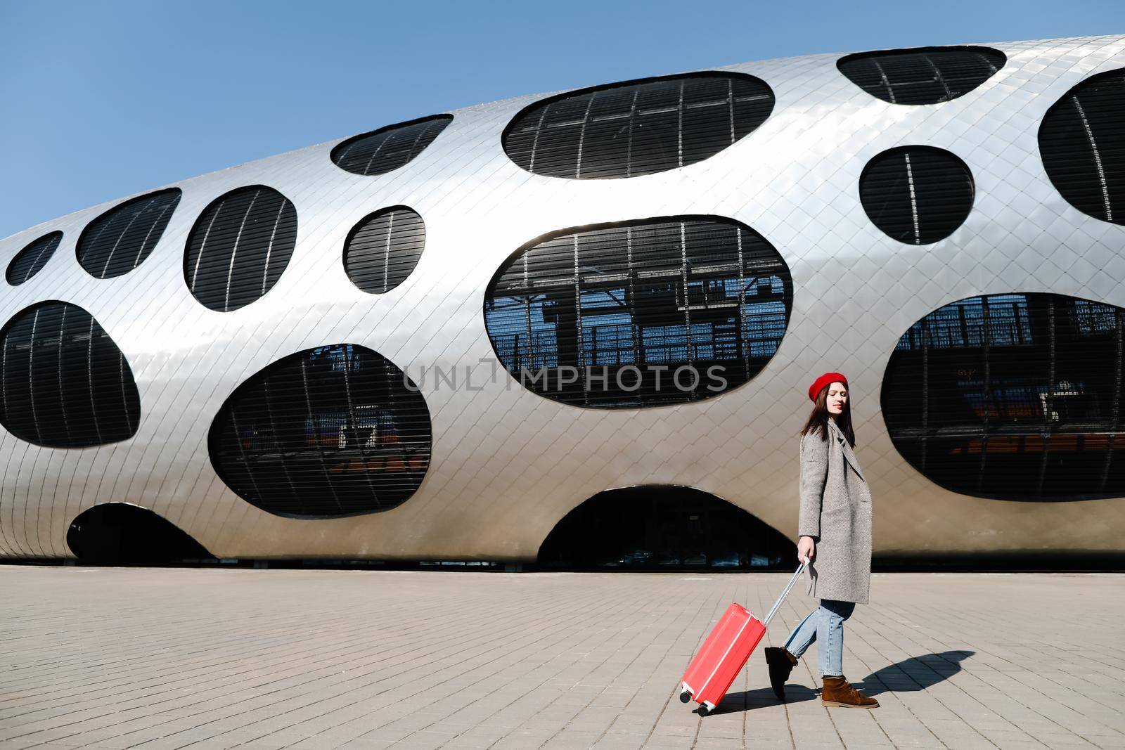 young woman with a red travel suitcase by the futuristic facade of modern architecture. Travel