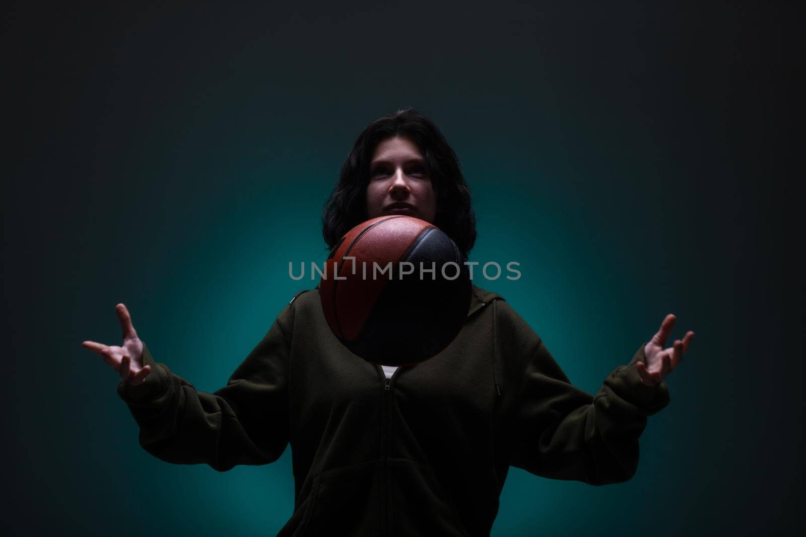 Teenage girl with basketball. Studio portrait with neon blue colored background.