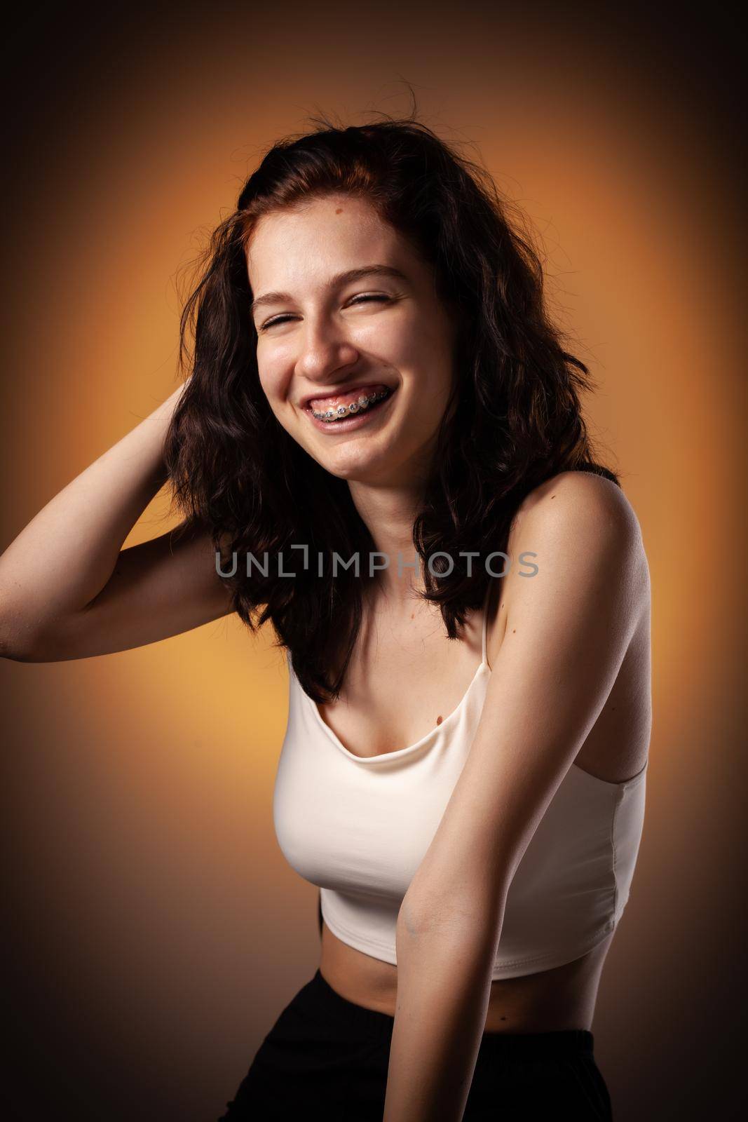 Teenage girl with dental braces. Studio portrait on neon orange colored background.
