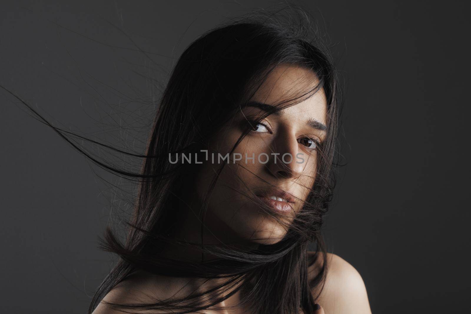 beauty fashion studio portrait of a beautiful young girl with windy hair in front of her face. by kokimk