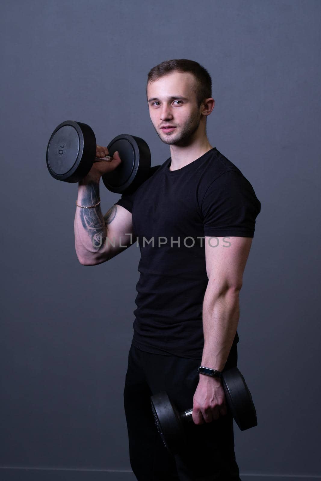 A guy with dumbbells in a black T-shirt muscular man sport posing, from aged headphones from fitness from athlete handsome, attractive t. Shirt biceps exercise, human young