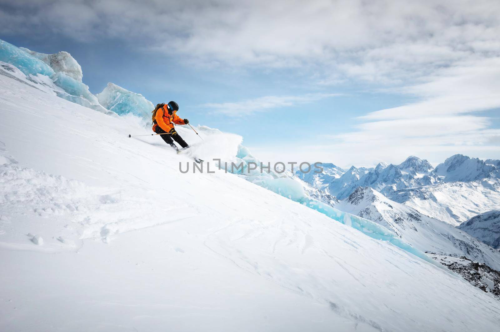 Professional skier ride at speed on a snowy slope against the backdrop of a glacier and high snow-capped mountains on a sunny day. Ski resort space copy presentation.