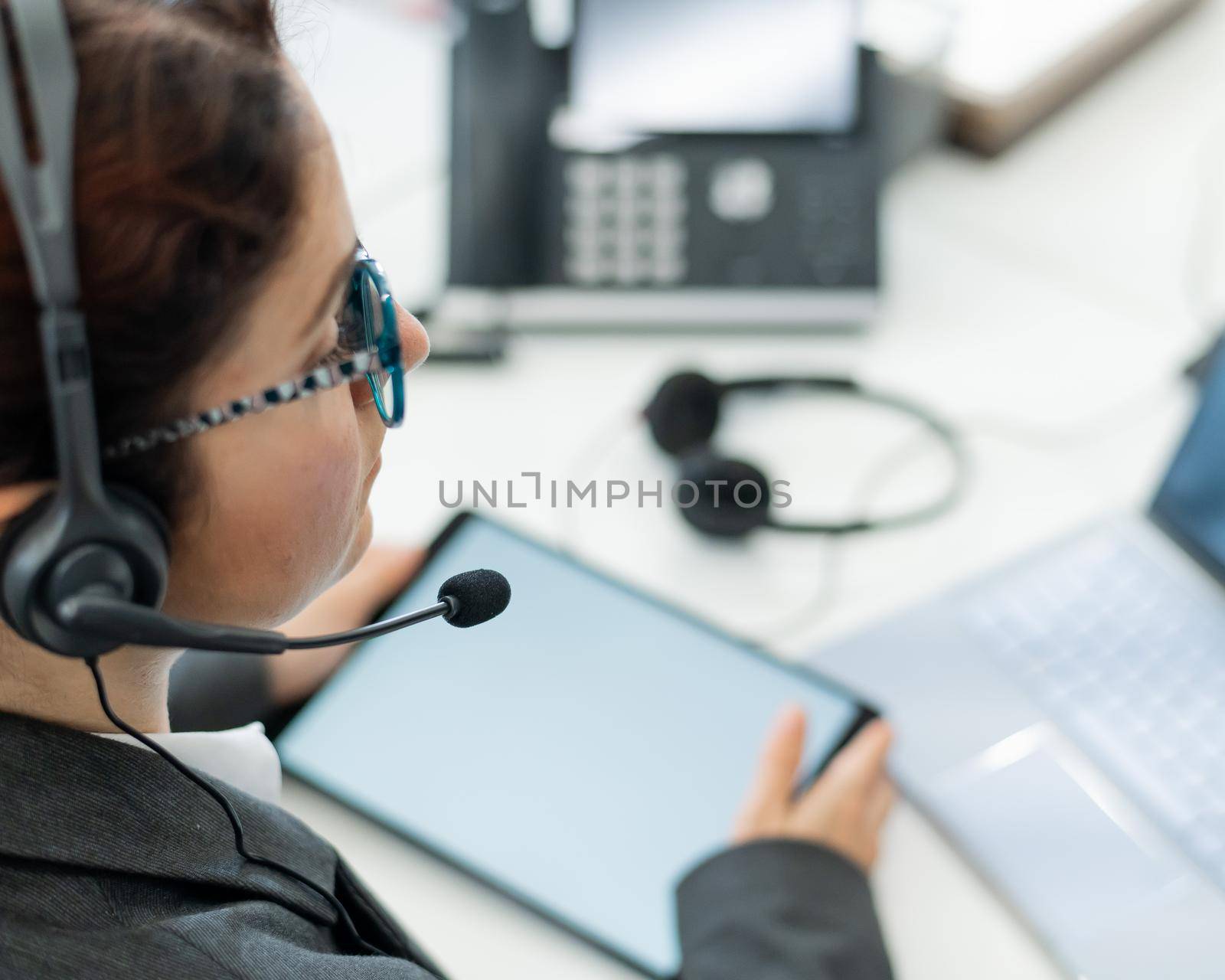 Rear view of a woman in a headset using a digital tablet while sitting at a desk. Friendly female support service operator at work