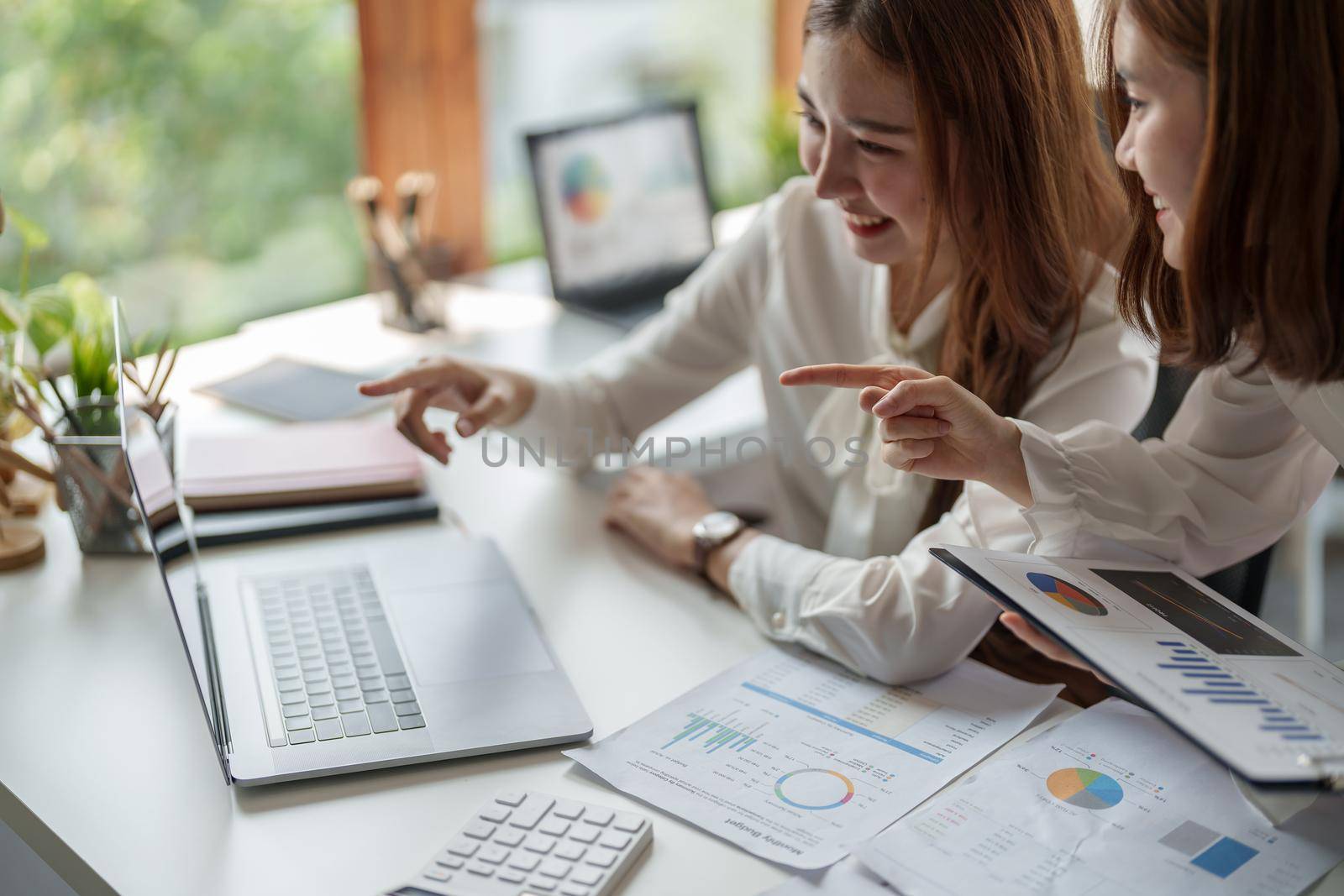 Two colleagues or students, asian girl are using a laptop while sitting at workplace discussing about job or education.