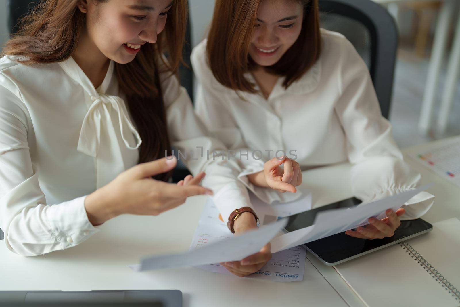 Two colleagues or students, asian girl working for financial paperwork while sitting at workplace discussing about job or education.