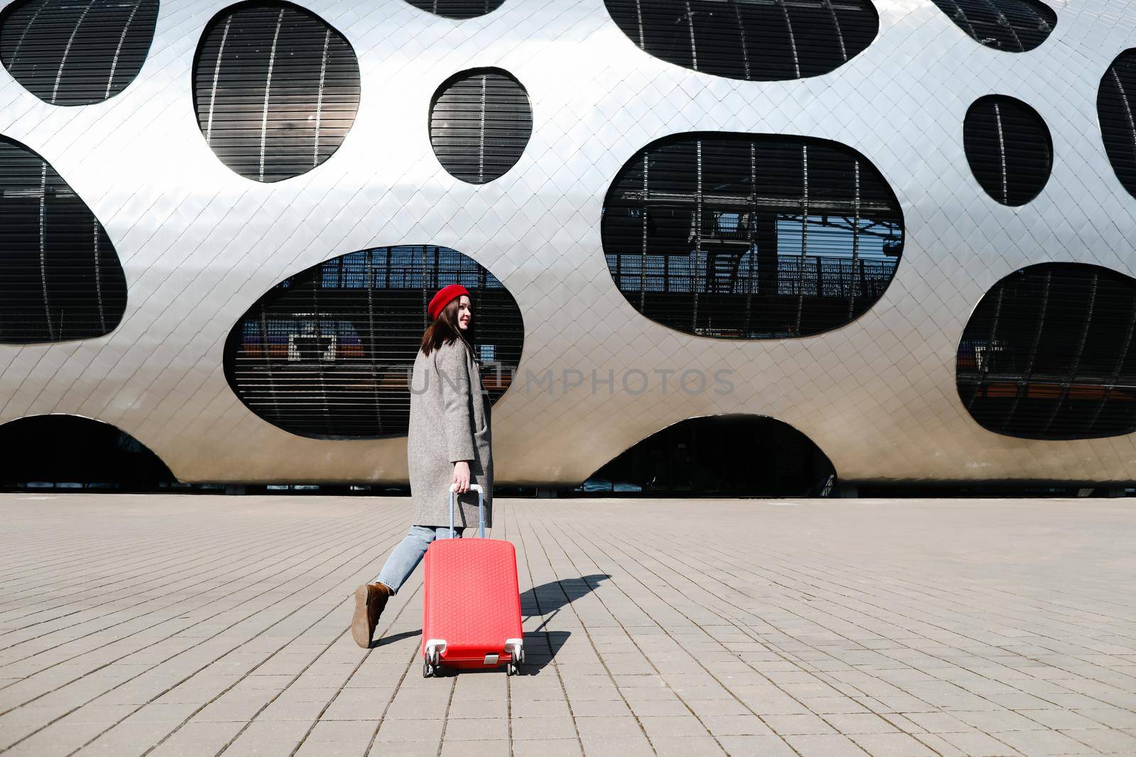 young woman with a red travel suitcase by the futuristic facade of modern architecture. Travel