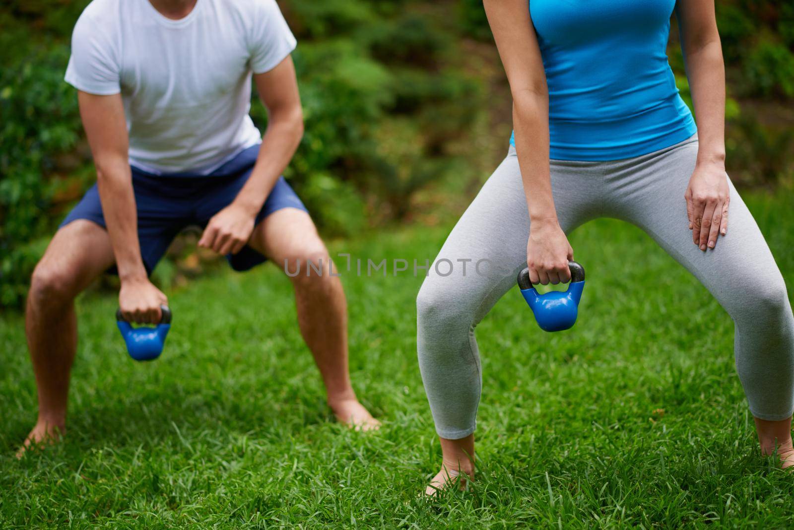 Working those muscles. Cropped shot of a man and woman using kettle bell weights in an outdoor exercise class. by YuriArcurs