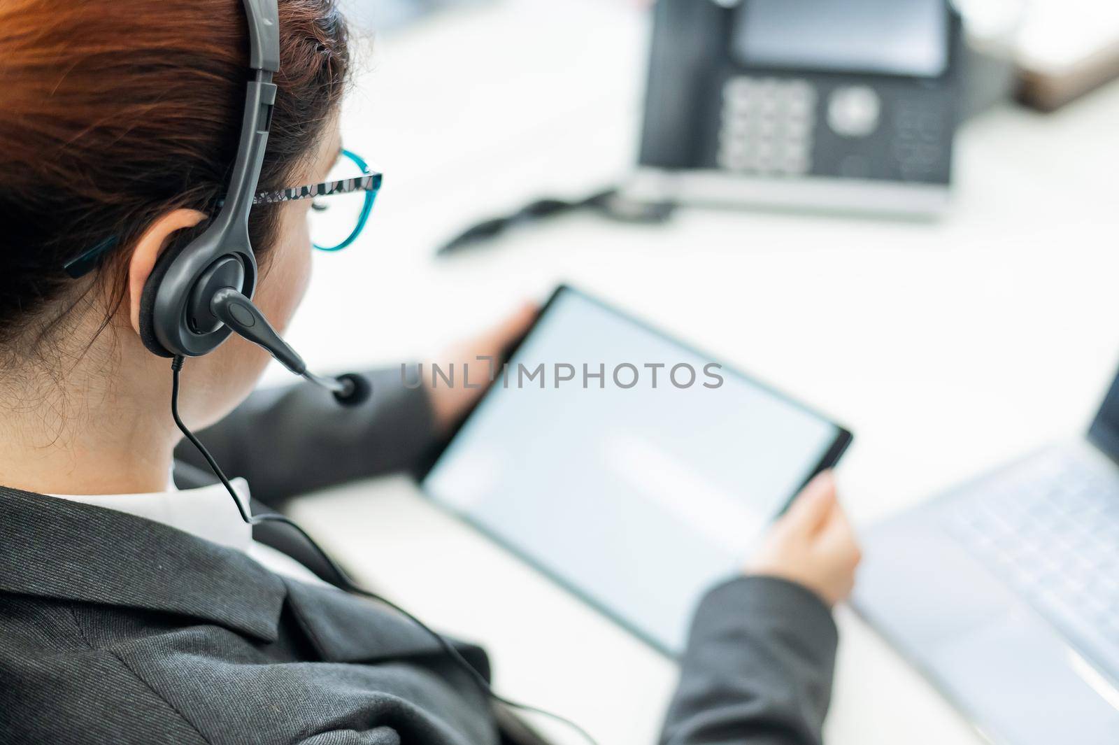 A business woman with a headset holds a digital tablet while sitting at a desk by mrwed54
